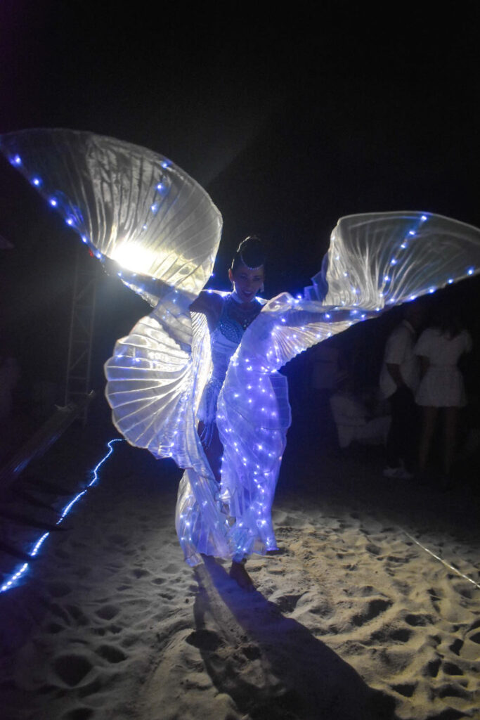 LED performance artist dancing on the beach at night in South Florida, wearing illuminated wings and glowing costume for a nighttime event by Aura Entertainment.